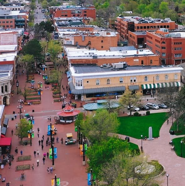 Aerial view of 17Walnut Boulder’s pedestrian street lined with trees, shops, and red brick buildings. People stroll wide paths as outdoor seating and greenery create a lively, vibrant urban scene.