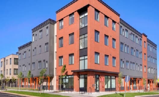 A modern, three-story apartment building—30Pearl Apartments Boulder—features red brick and gray siding, large windows, and a clean sidewalk in front, all beneath a clear blue sky.