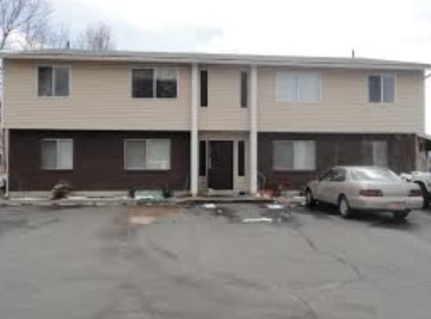 Auburn Heights 4-plex Logan: This two-story apartment building features a brown brick lower half and beige siding above. Several windows and a central entrance overlook a cracked asphalt lot with parking in front.