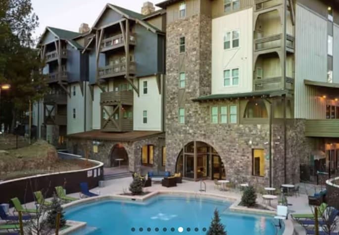 Fremont Station Flagstaff is a modern mountain lodge-style hotel with stone and wood siding overlooking an outdoor swimming pool surrounded by lounge chairs, small trees, balconies, and large windows.