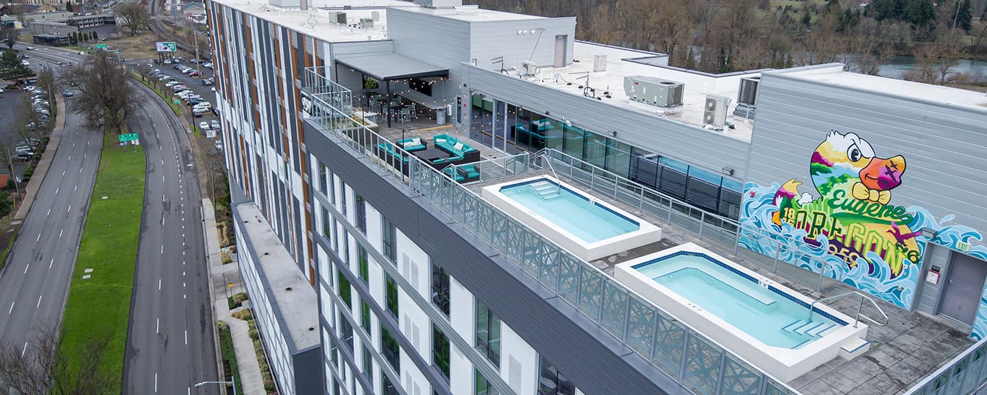 959 Franklin is a modern multi-story apartment building set beside a road, surrounded by trees and greenery under a partly cloudy sky.