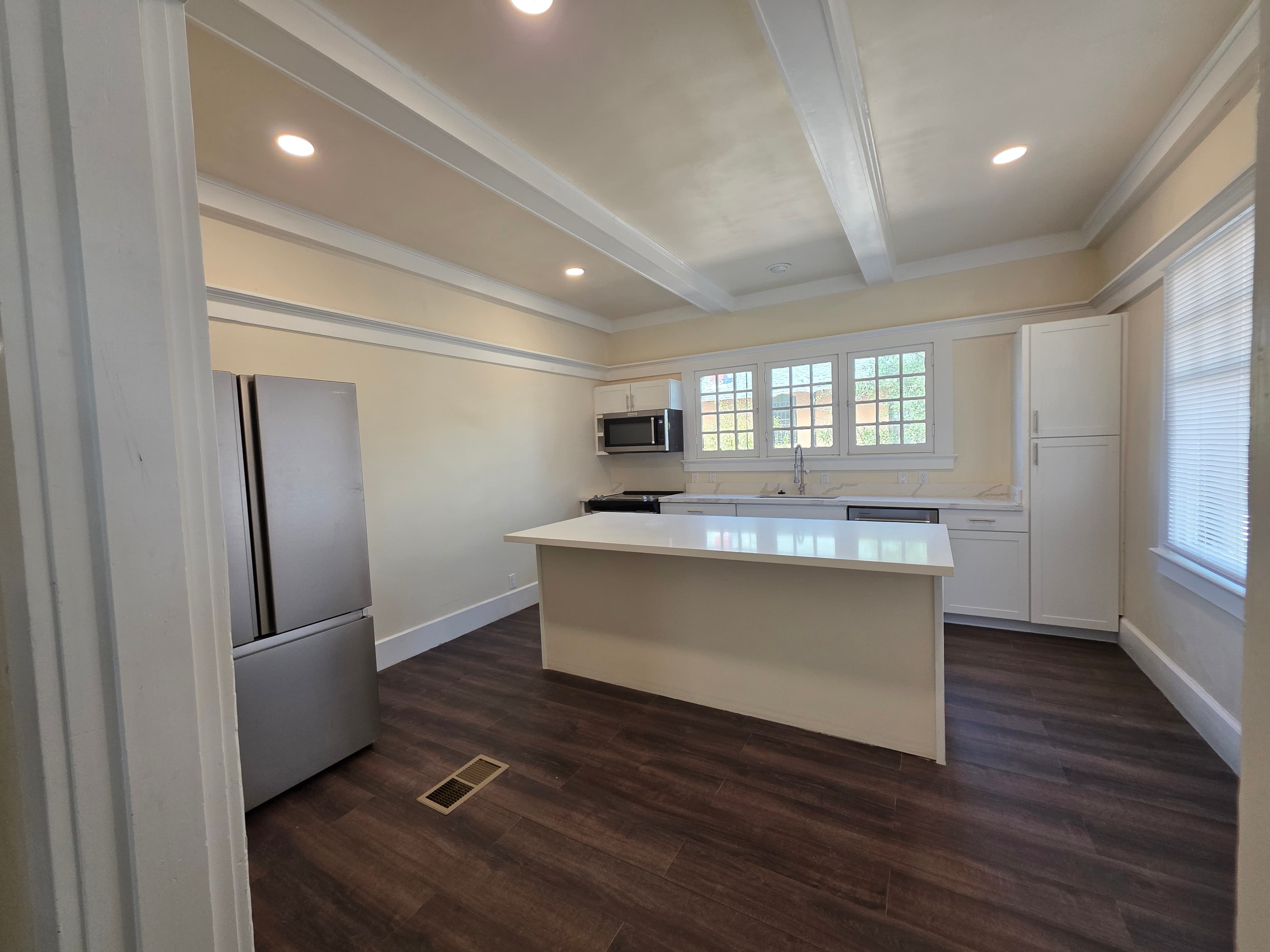 A modern kitchen at 833 N 4th Ave features white cabinets, stainless steel appliances, a large center island, and dark wood flooring. Sunlight enters through multiple windows, brightening the space.
