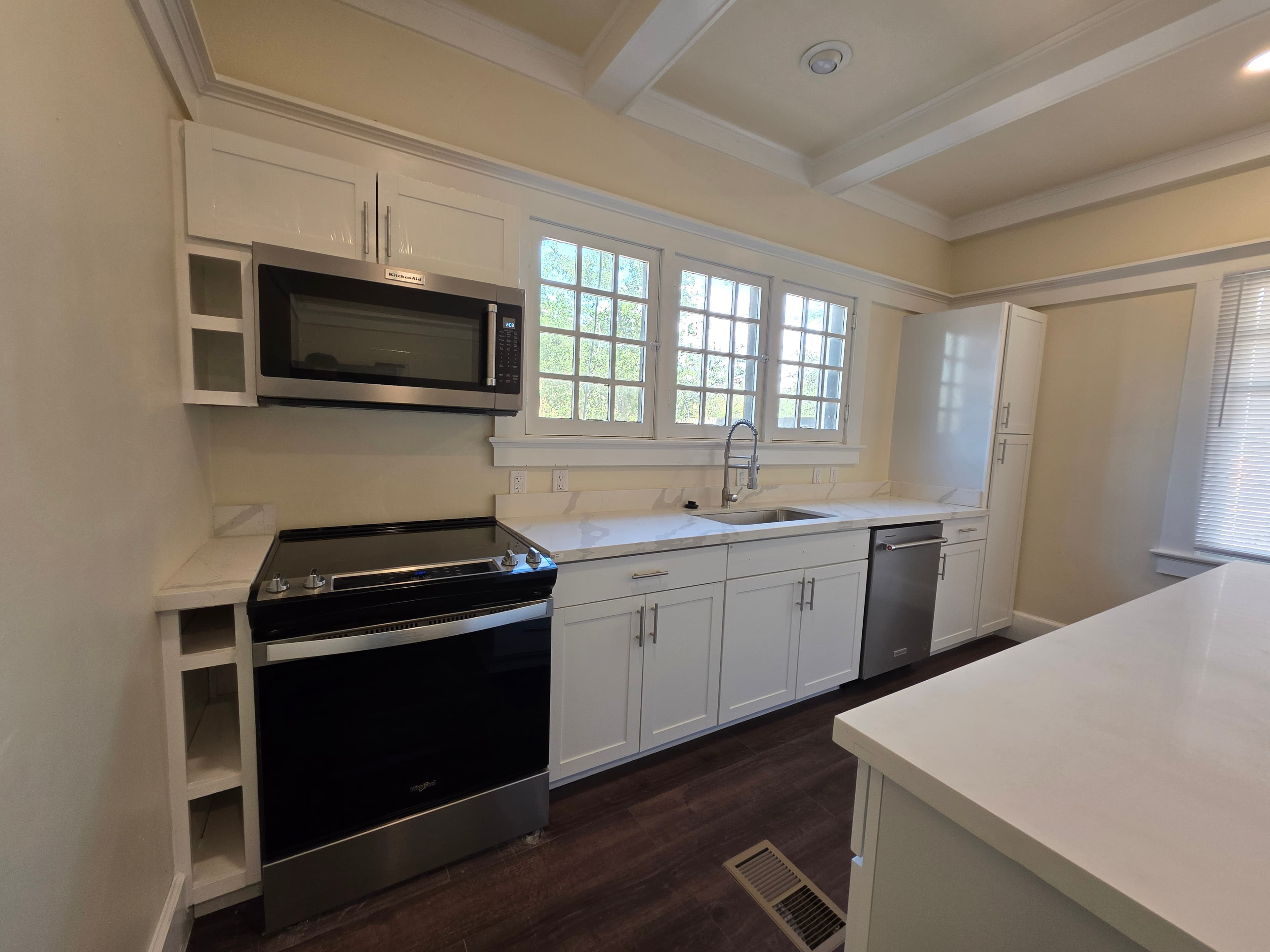 A modern kitchen at 833 N 4th Ave features white cabinets, a black stove, built-in microwave, dishwasher, large sink, and multiple windows above the countertop. The space boasts dark wood flooring and bright natural light.