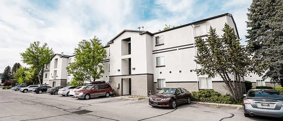 The Crestwood Provo is a three-story apartment building with a white and gray exterior, surrounded by trees. Several parked cars line the parking lot in front under a partly cloudy sky.