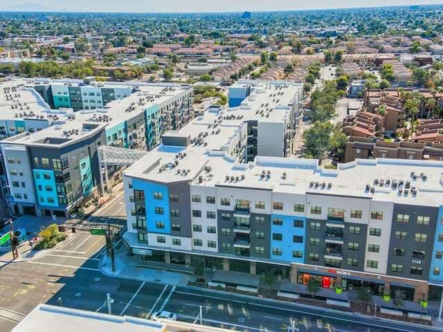 Aerial view of modern apartment buildings with white and blue facades in an urban area, including Park Place Tempe, surrounded by streets, trees, and residential houses, with mountains visible in the background.