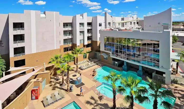 Alight Tempe offers a modern hotel-like complex with multiple floors, two outdoor swimming pools, a hot tub, lounge chairs, palm trees, and blue skies—perfect for student apartments in Tempe AZ.
