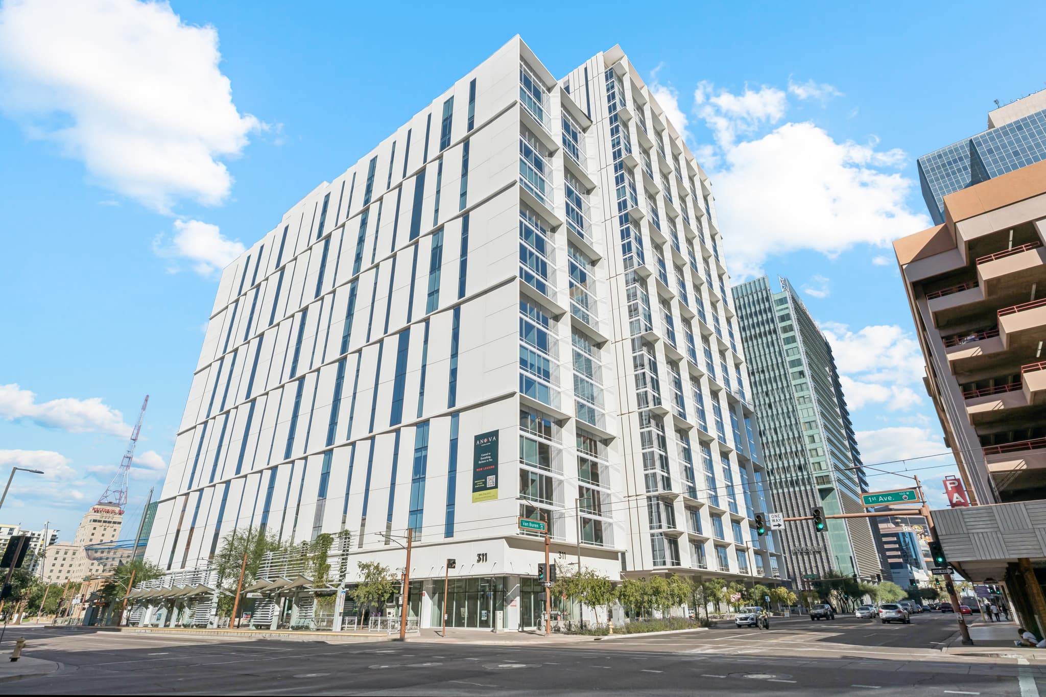 A modern multi-story office building with white exterior panels and large windows stands near Central Station at a street corner in an urban downtown area under a blue sky with scattered clouds.