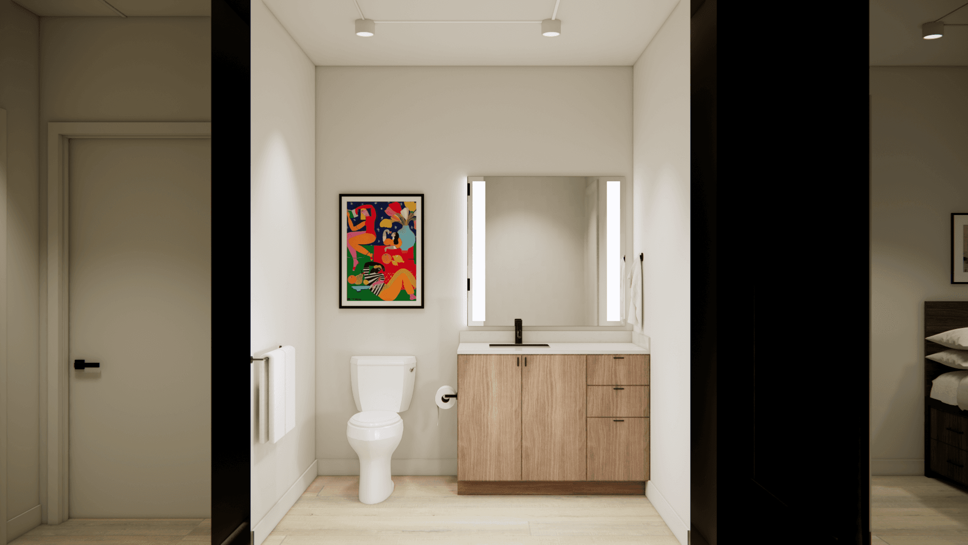 A modern bathroom at Yugo Salt Lake City features light wood flooring, a white toilet beside a vanity with a wood cabinet, large mirror, wall art above the toilet, towel rack, and soft overhead lighting.