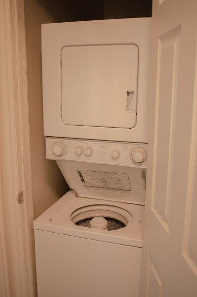 In this Carolina Townhomes Logan unit, a stacked washer and dryer set fits neatly in a small closet. The washing machine lid is open, revealing the drum, while the dryer above remains closed and the closet door is partially ajar.
