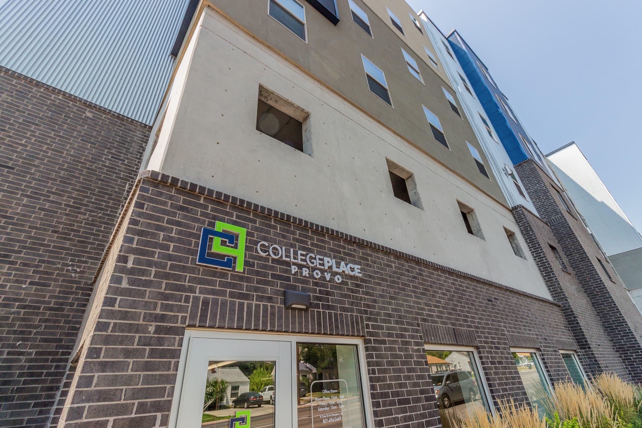 The photo shows the exterior of CollegePlace Provo, a modern multi-story building featuring a sign above the entrance. The facade combines sleek dark brick with light-colored concrete for a contemporary look.
