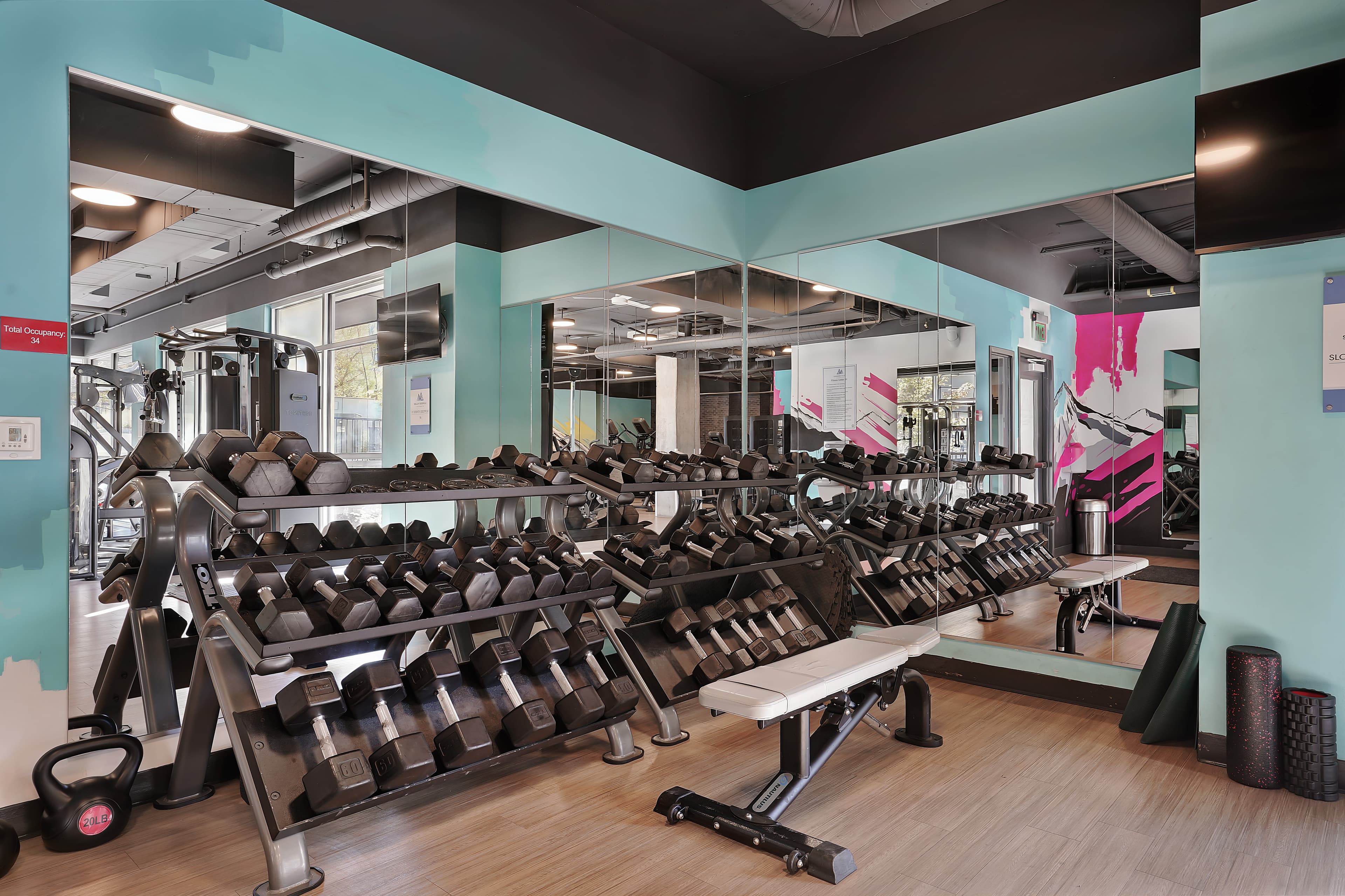 A gym at Slopeside Village in Park City, featuring racks of dumbbells, a weight bench, kettlebells, foam rollers, and large wall mirrors reflecting the bright, modern space with exercise machines in the background.