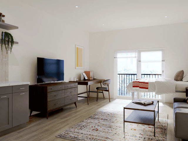 Modern studio apartment at Ivory University House Salt Lake City with light wood floors, a bed by large windows, a TV on a wooden dresser, a desk, patterned rug, coffee table, and neutral decor. Natural light fills the room.