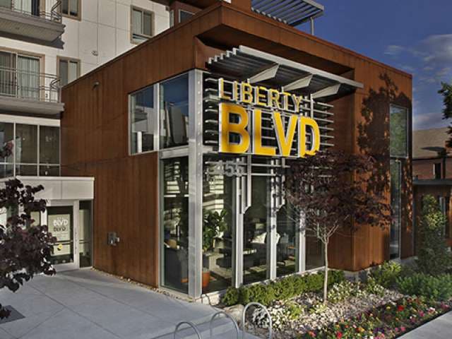 Modern building with large glass windows and a prominent yellow “LIBERTY BLVD” sign above the entrance, surrounded by landscaped greenery and a paved walkway in the heart of Liberty Blvd, Salt Lake City.