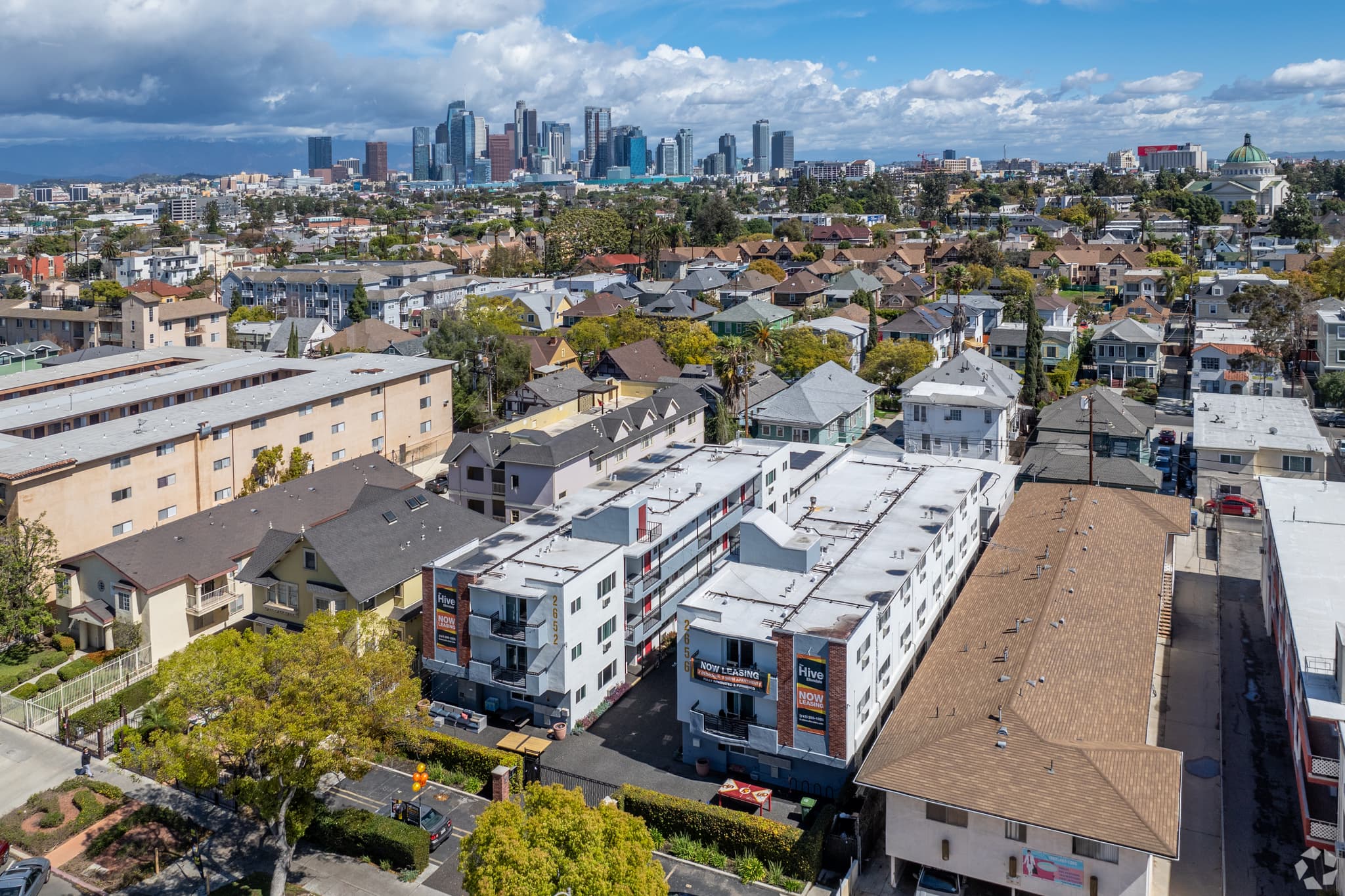 An aerial view of a dense Los Angeles neighborhood with Hive Ellendale prominently nestled in the foreground and a distant cityscape beyond.