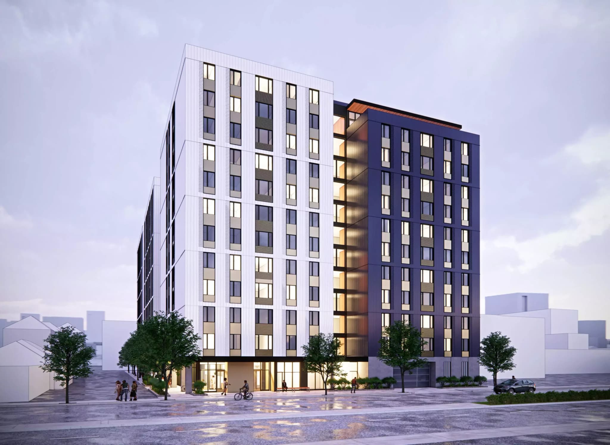 Union on Broadway features a modern multi-story apartment building with white and dark gray sections, large windows, and illuminated interiors. A few trees and people are visible in front, and the ground appears wet from recent rain.