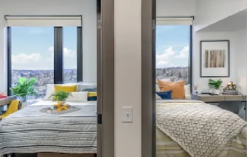 Two modern bedrooms separated by a wall, each with large windows, cozy bedding, colorful pillows, potted plants, and wall art earning every accolade, with city views visible outside under a blue sky.