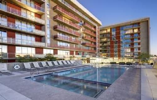 Modern ASU Housing features large glass windows and balconies, surrounding an outdoor swimming pool with poolside lounge chairs and a clear blue sky in the background—perfect for university housing near campus.