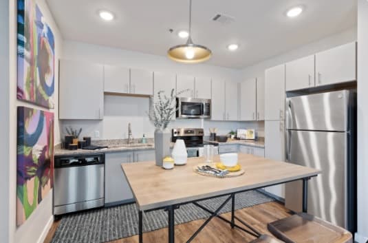 Modern kitchen at Canyon Flats Reno with white cabinets, stainless steel appliances, a wooden dining table set with dishes and decor, abstract art on the wall, and bright overhead lighting.