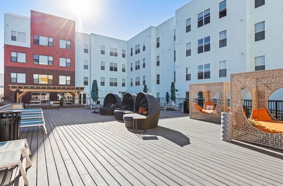Sunny outdoor lounge area at Canyon Flats Reno features modern patio seating, orange swing chairs in wooden cabanas, lounge chairs, and a pergola, all surrounded by multi-story apartment buildings.