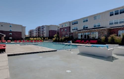 Grove Apartments offers a modern complex featuring a large outdoor swimming pool with poolside lounge chairs and red cushioned seating areas, surrounded by multi-story buildings under the clear Pullman sky.