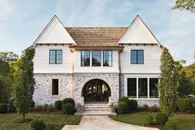 A two-story house on FM Eastwood Court with white siding and stone accents, featuring a central arched entryway, large windows, and a landscaped front yard with trees and shrubs.