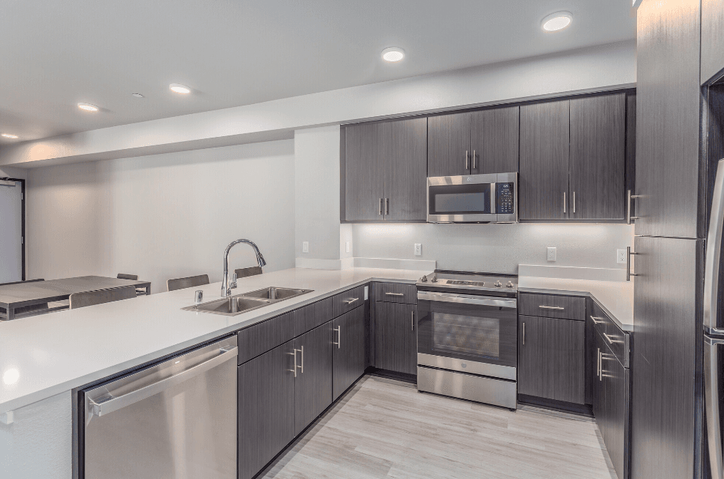 Modern kitchen with dark wood cabinets, stainless steel appliances, white countertops, a built-in microwave, electric stove, dishwasher, sink with faucet, and recessed ceiling lights. Light-colored flooring.