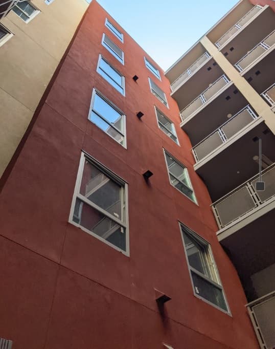 Upward view of two modern apartment buildings, including Jefferson Flats with its red-brown facade and rectangular windows, and another light-colored building with balconies, set against a clear blue sky.