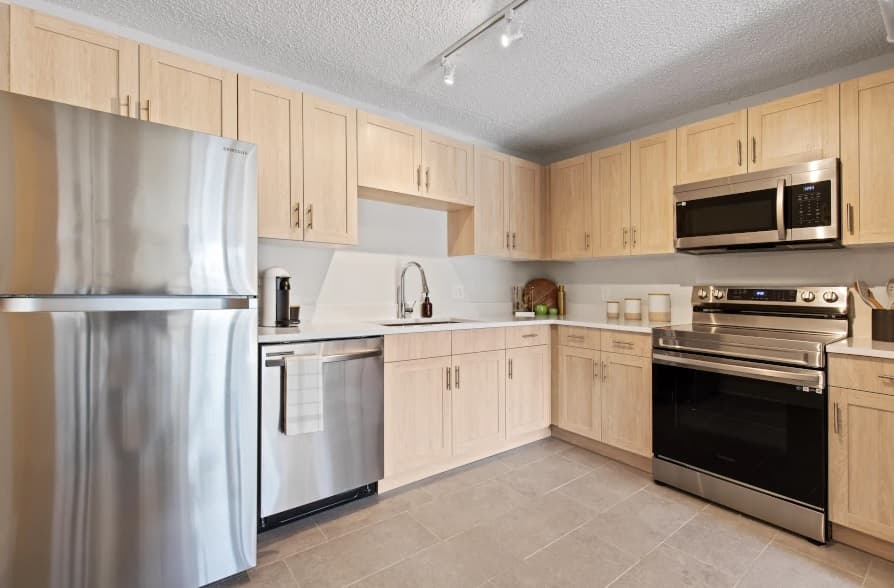 Modern Mountainaire Boulder kitchen with light wood cabinets, stainless steel appliances—including refrigerator, dishwasher, and oven with microwave above. Neutral tile flooring and under-cabinet lighting create a clean, contemporary Boulder vibe.