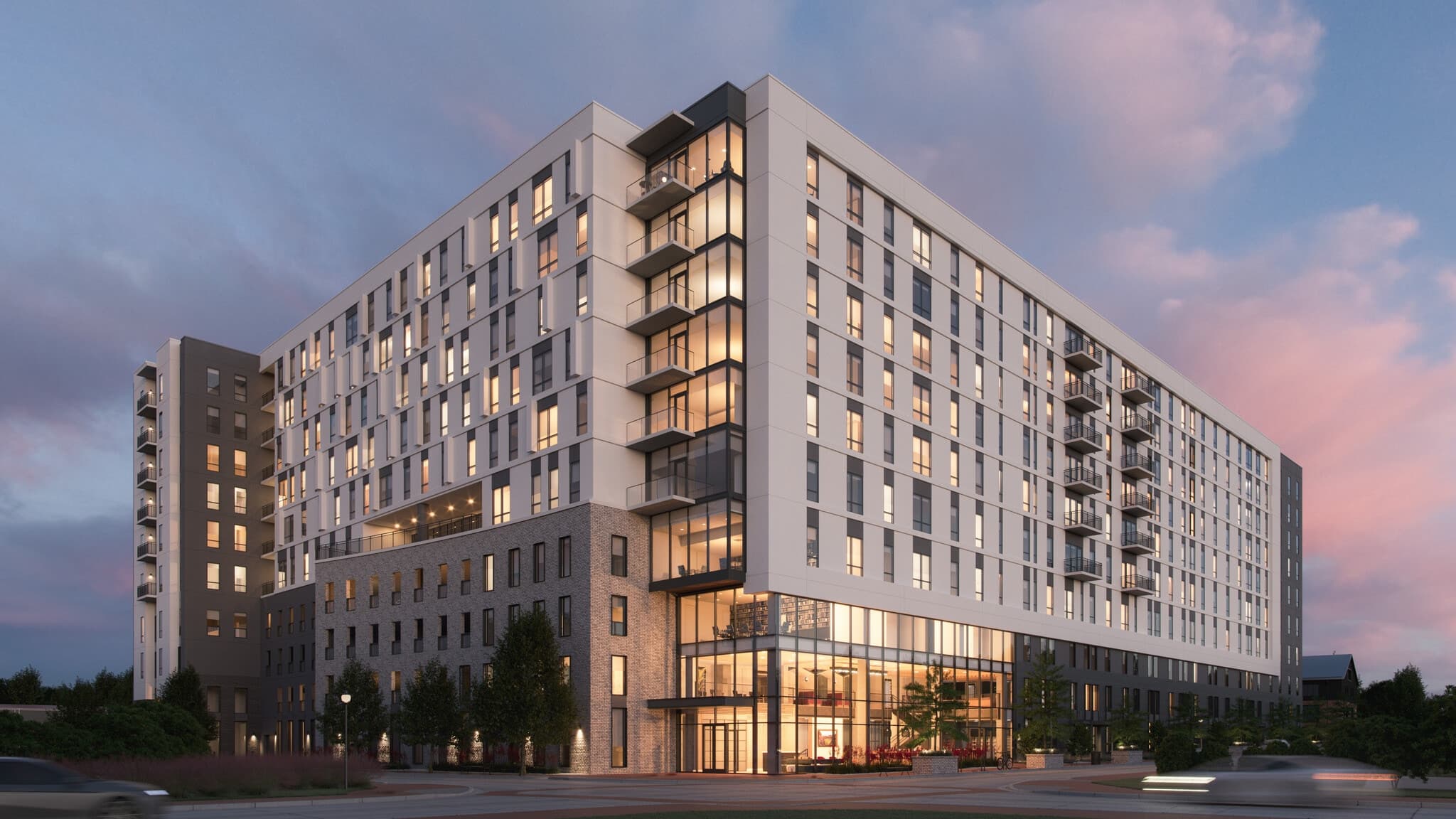 The Otto Northgate is a modern, multi-story apartment building with large windows and balconies, lit from within at dusk. Cars and trees line the foreground, set against a serene pink and blue sky.