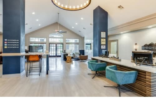 Spacious, modern office lobby at The Highlands Reno with high ceilings, contemporary furniture including teal chairs, a long reception desk, and a large circular chandelier. Natural light streams in through large windows and glass doors at the back.