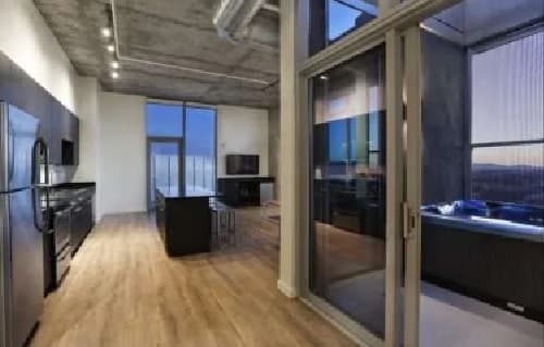 Modern kitchen with stainless steel appliances, wooden floor, and a central island. At University House Tempe, large windows and glass doors open to a balcony with a hot tub, offering stunning sunset and cityscape views.