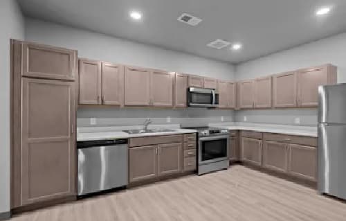 Modern kitchen in this Union at Pacific Highway apartment features light wood cabinets, stainless steel appliances, white countertops, and light wood flooring. The space is well-lit with recessed ceiling lights for a bright, contemporary feel.