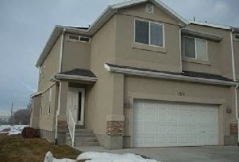 Charming two-story beige house at 1314 S 1410 E Provo with a double garage, white trim, and stone accents. Snow covers the ground, and a small set of stairs leads to the front door on the left side.