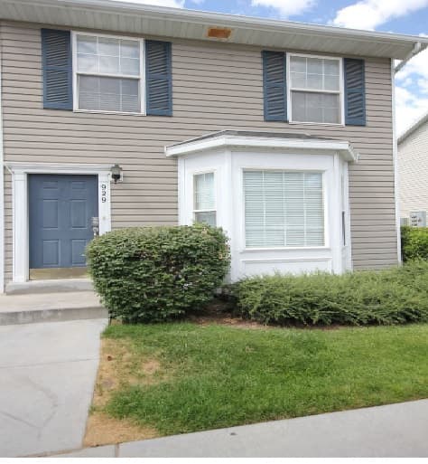 Located at 929 North 1760, Provo, this two-story house features gray siding, blue shutters, and a blue front door. A large window with white trim, green shrubs, and a small lawn create inviting curb appeal by the entrance.