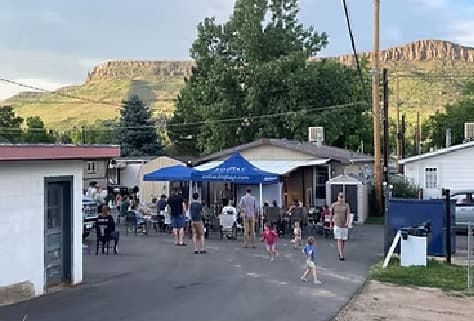 Residents of Pinewood Apartments Boulder, including families and children, gather outside around tables and under a blue tent in a residential area with mountains in the background.