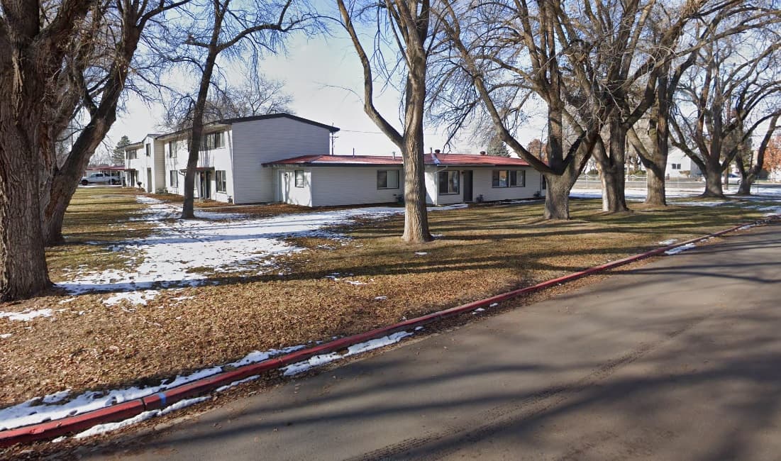 Two white, single-story and two-story buildings in Harrisville Heights Ogden are surrounded by leafless trees and patches of snow on the ground, next to a paved road on a winter day.