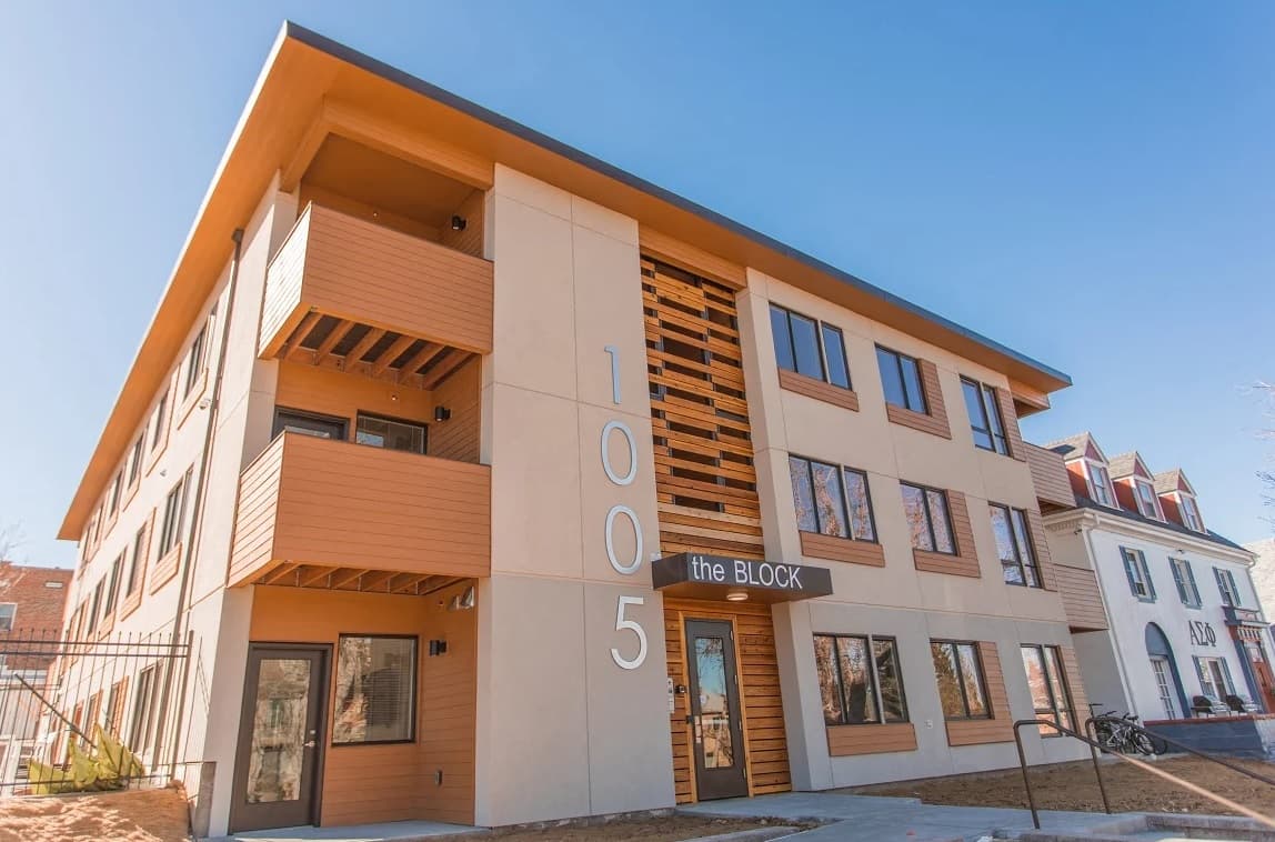 A modern three-story apartment building with wood accents and balconies, The Block Boulder features large numbers 1005 displayed vertically on the front and a sign that reads the BLOCK. The sky is clear and blue.