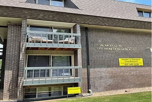 A three-story brick townhouse building with balconies and a yellow sign advertising vacancies. The sign reads Vacancy & Campus Townhouses with a phone number. Amherst Townhouses is partially visible, near Boulder Commons commercial offices and retail.