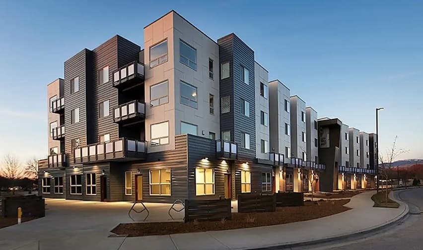 The 951 Boise is a modern four-story apartment building with large windows and balconies, featuring dark and light exterior panels, located beside a curved sidewalk at sunset.