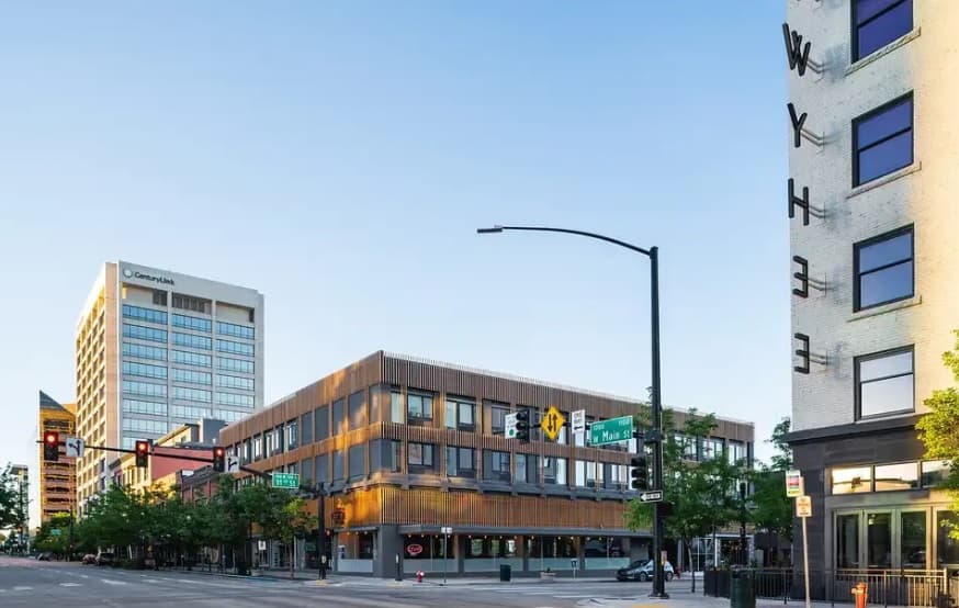 A city street corner with modern buildings, including a three-story wooden facade building, a high-rise with a Central Park sign, and The B Side Boise featured near a white building with WYTHE in large letters. Traffic lights and street signs are visible.