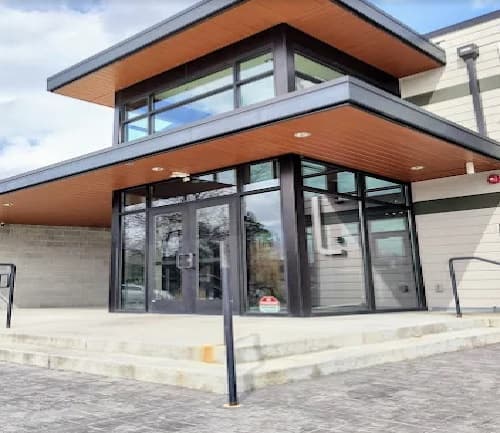 Modern building entrance at Creek Bend Apartments Boise, featuring large glass windows, double glass doors, a flat roof overhang, and wide stone steps with metal railings on both sides.
