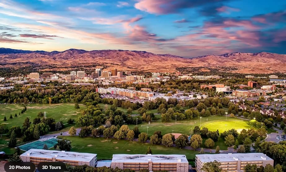 Aerial view of a city nestled among green trees and parks, with Parkview Apartments Boise standing amid a cluster of buildings in the center and mountains in the background under a colorful, partly cloudy sky at sunset.