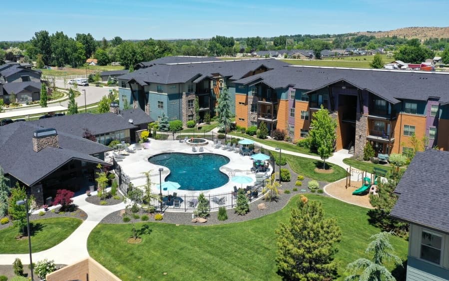 Aerial view of Retreat at Silvercloud Boise, a modern apartment complex featuring a central outdoor swimming pool, lounge chairs, green lawns, landscaped gardens, and surrounding residential buildings.