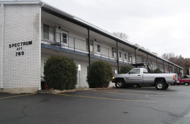 A two-story white brick Spectrum 2 bedroom apartment building in Logan, labeled Apt. 760, with bushes in front and a silver pickup truck parked in the lot on a cloudy day.