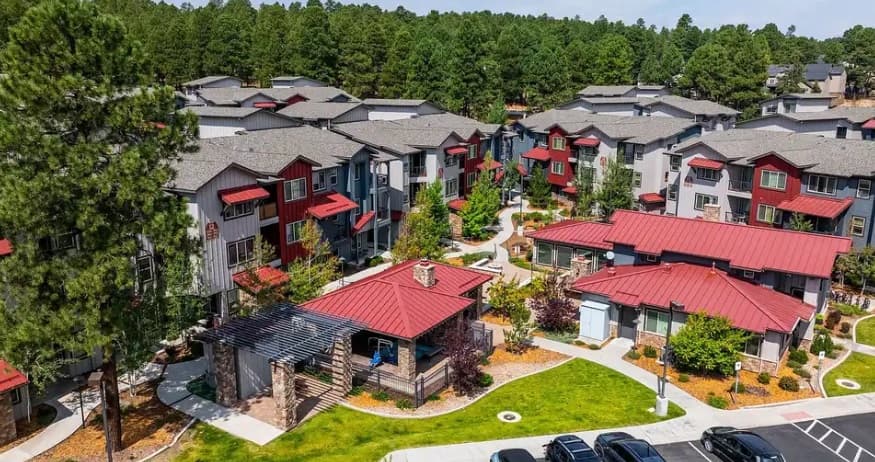 Aerial view of a residential complex with multiple modern buildings featuring red roofs, surrounded by trees and landscaped paths, set near the scenic Mountain Trail Flagstaff and bordered by a lush forested area.