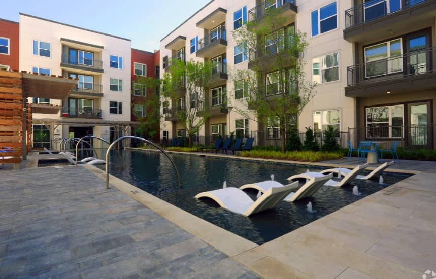 Modern courtyard at Union at River East Apartments Fort Worth features a rectangular swimming pool, in-water lounge chairs, poolside seating, and lush trees—surrounded by multi-story buildings with balconies.