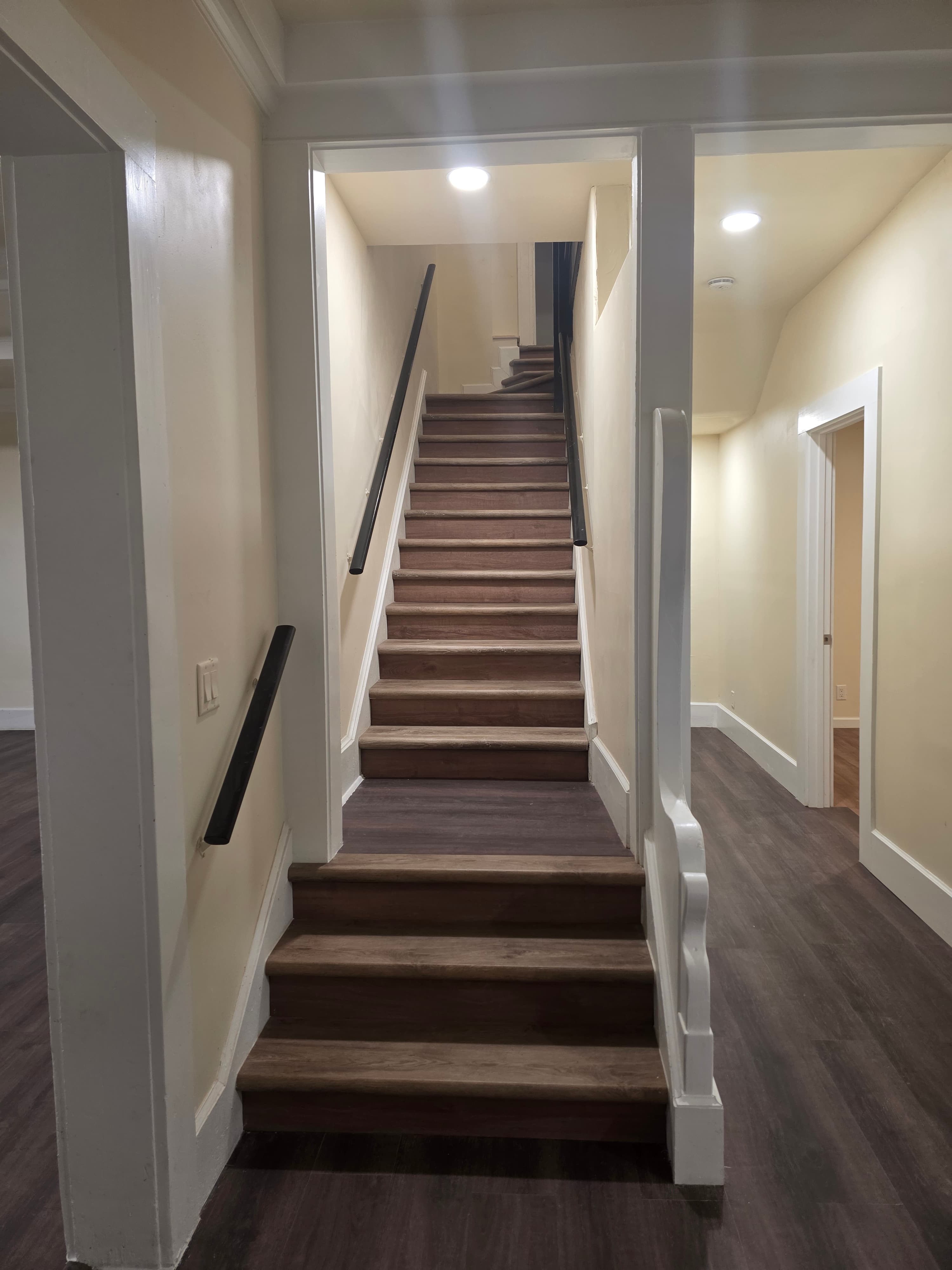 A wooden staircase with dark handrails on both sides leads up to a well-lit hallway at 833 N 4th Ave. The cream-colored walls and dark wood floor complement doorways to adjoining rooms visible on either side.