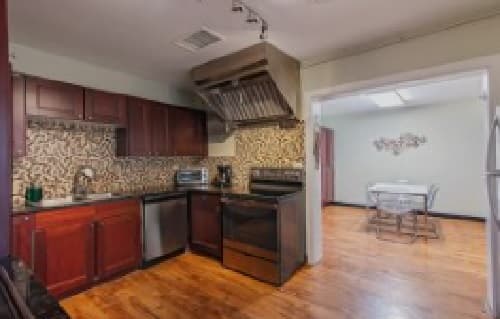 A kitchen at 909 14th Boulder features dark wood cabinets, stainless steel appliances, a patterned tile backsplash, and hardwood floors, with an adjacent dining area visible through an open doorway.