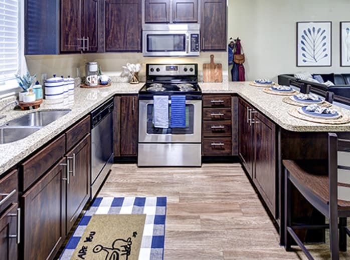 A modern kitchen at U Club Townhomes with dark wood cabinets, stainless steel appliances, granite countertops, and blue-themed decor creates a stylish student housing option near Marion Pugh. Blue-striped towels and a decorative rug add cozy touches.
