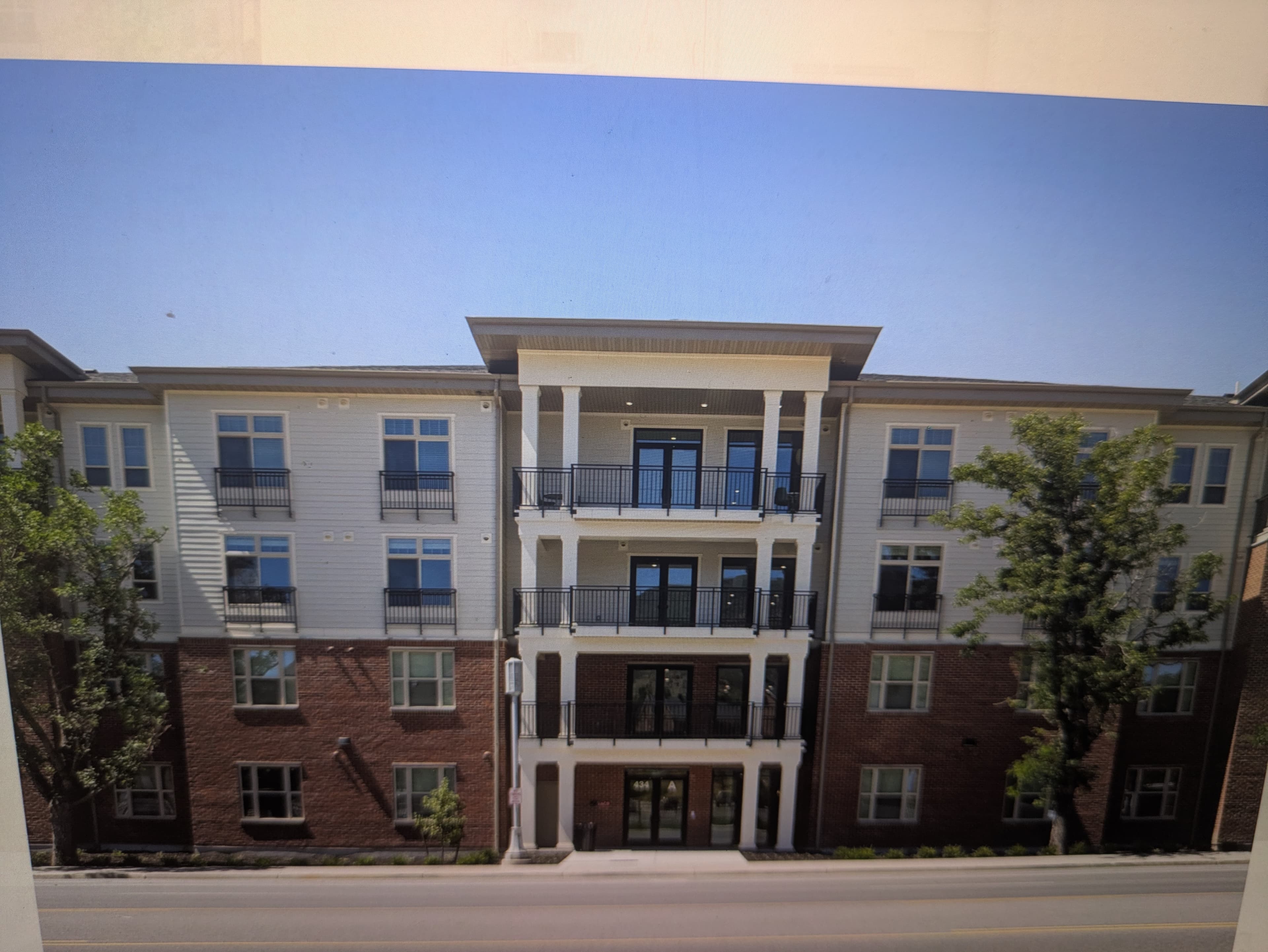 Four-story Ivory University House Salt Lake City apartment building with a brick facade on the lower levels, white siding on the upper stories, black roof, balconies, and trees out front, set against a cloudy sunset sky.